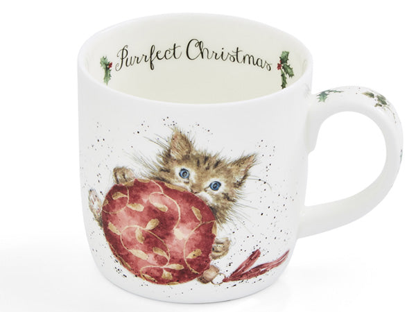 A white ceramic mug featuring a watercolor illustration of a brown tabby kitten with blue eyes holding a large red ornament. The inside of the mug is printed with the text 'Purrfect Christmas' in black script, and the handle is decorated with small holly motifs.
