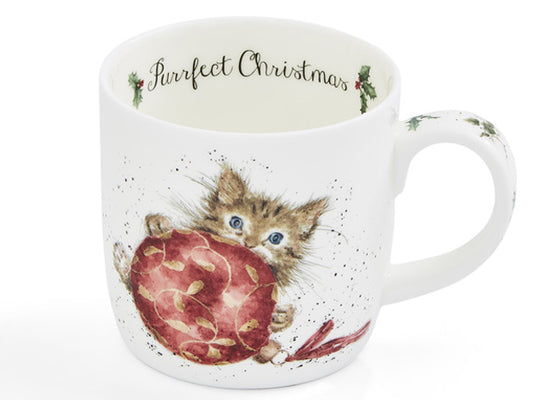 A white ceramic mug featuring a watercolor illustration of a brown tabby kitten with blue eyes holding a large red ornament. The inside of the mug is printed with the text 'Purrfect Christmas' in black script, and the handle is decorated with small holly motifs.
