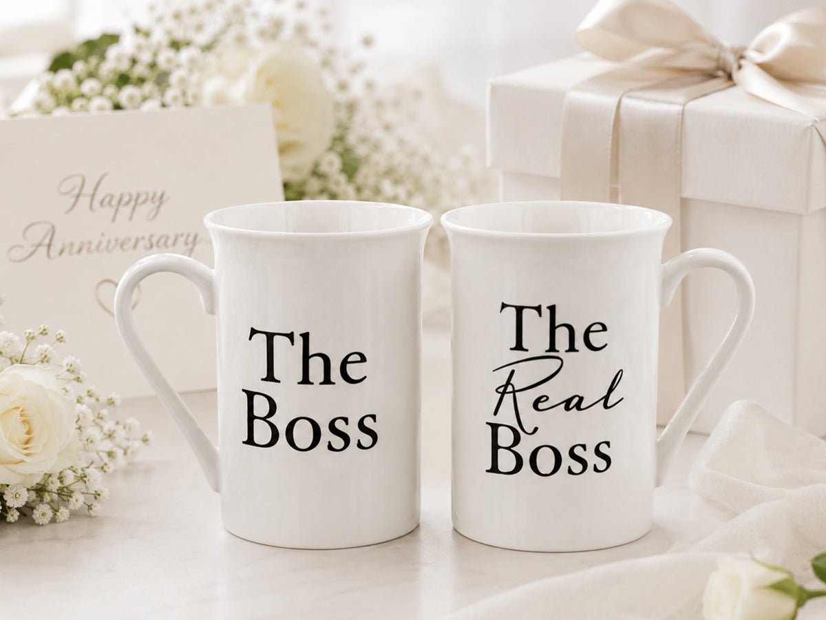 Two white mugs with 'The Boss' and 'The Real Boss' text on a decorative background with flowers and gift boxes.