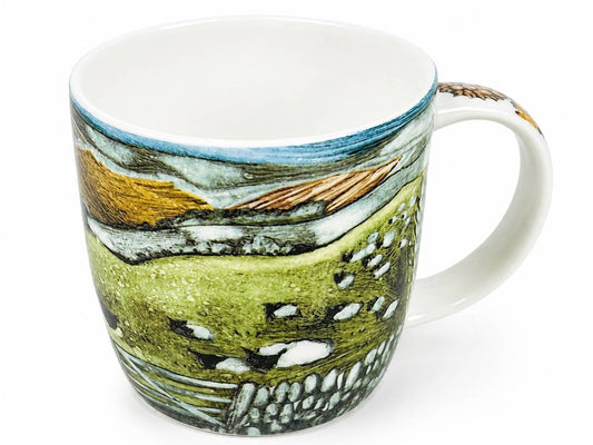A white ceramic mug featuring a detailed landscape illustration with green hills, blue sky, and golden fields.