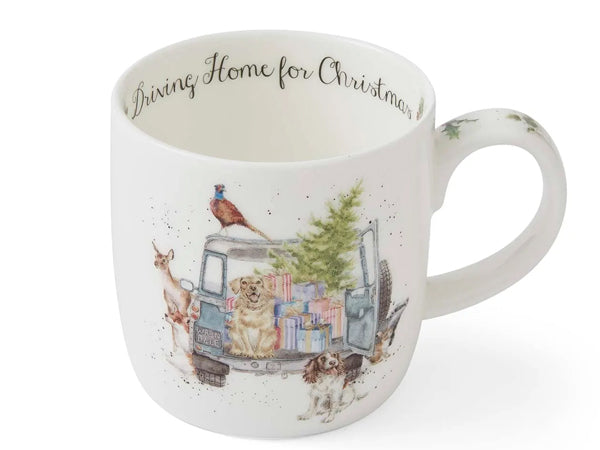 A white ceramic Christmas mug featuring an illustration of a blue van filled with presents, a Christmas tree, and dogs, with the text 'Dining Home for Christmas' printed inside the rim.