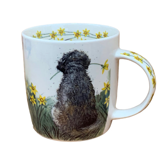 The Alex Clark mug features a charming Doodle dog enjoying the view while holding a daffodil in its mouth. Additionally, daffodil flower illustrations adorn the inside rim and down the handle of the mug, adding to its delightful appeal.