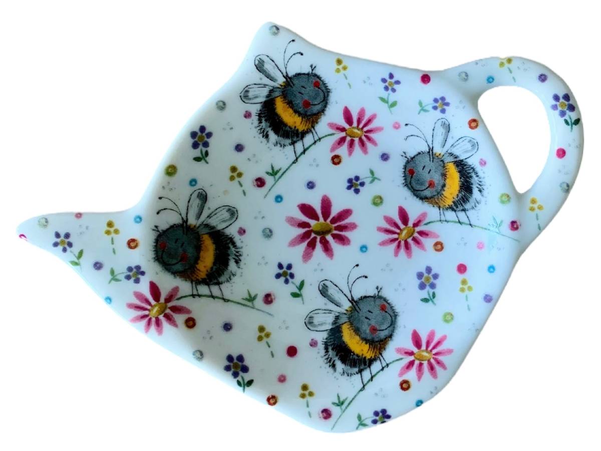 A white ceramic teapot-shaped dish decorated with a whimsical pattern of smiling bees and colorful flowers, shown on a plain white background.