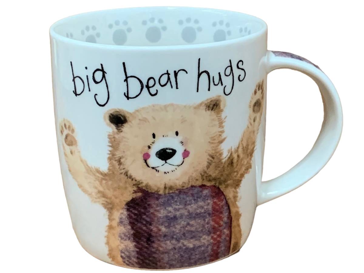 The Alex Clark mug features an illustration of a friendly bear with its arms open for a welcoming hug, accompanied by the words "big bear hugs" on the top of the mug. Enhancing its design, the mug includes a bear paw illustration around the inside rim and illustrations down the handle.
