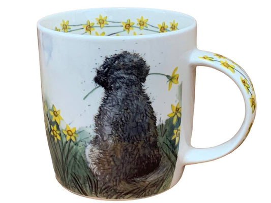 The Alex Clark mug features a charming Doodle dog enjoying the view while holding a daffodil in its mouth. Additionally, daffodil flower illustrations adorn the inside rim and down the handle of the mug, adding to its delightful appeal.