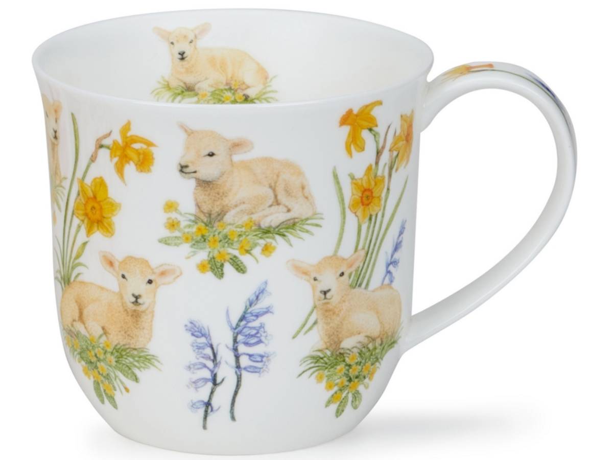 A white ceramic mug decorated with a pattern of light brown lambs and yellow daffodils, with a small blue bellflower near the bottom, set against a plain white background.
