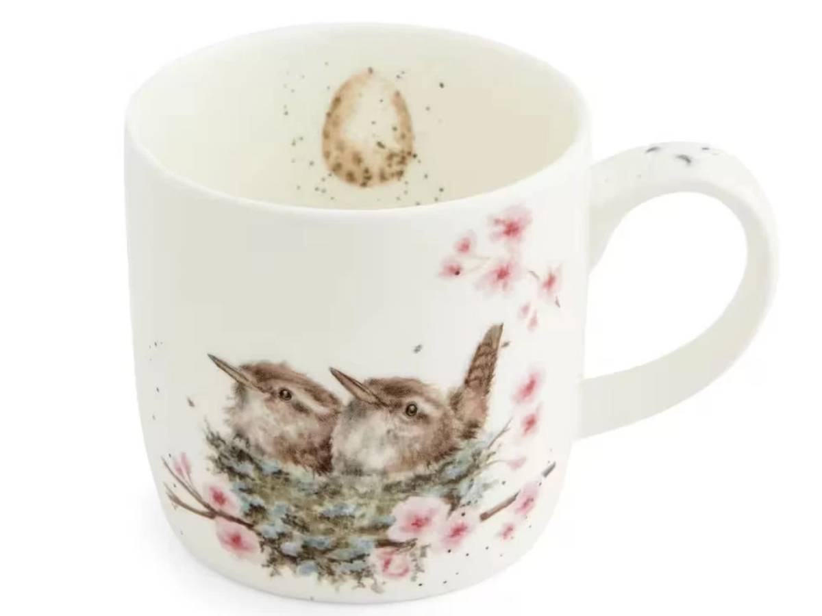 A white ceramic mug featuring a watercolor-style illustration of two wrens in a nest with pink blossoms, shown on a plain white background.