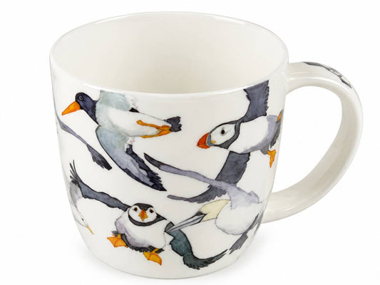A white ceramic mug decorated with a watercolor-style print of puffins in flight, featuring black, white, gray, and orange details, set against a plain white background.