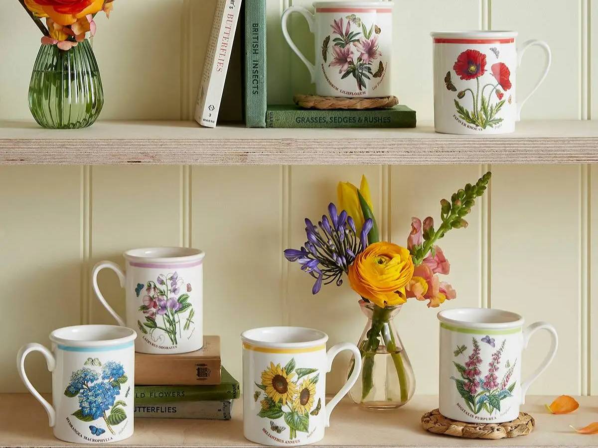 Decorative mugs with floral designs on a shelf against a light-colored wall.