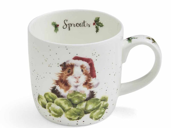 A white ceramic mug with a speckled finish, featuring a watercolor illustration of a guinea pig wearing a Santa hat sitting on Brussels sprouts. The inside of the mug is printed with the word 'Sprouts' and holly accents.