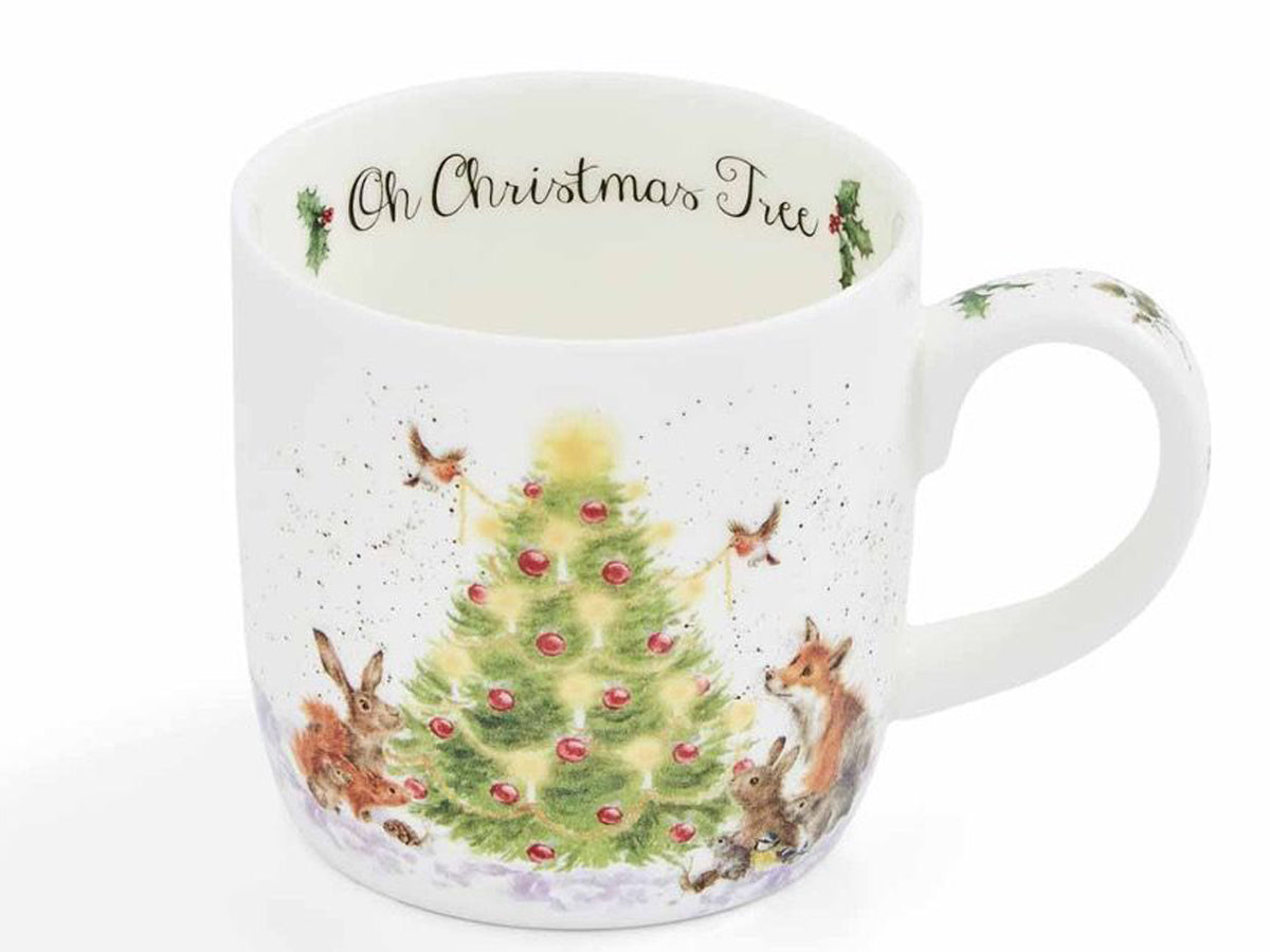 A white ceramic Christmas mug featuring a watercolor illustration of a decorated Christmas tree with rabbits, a fox, birds, and snow. The inside of the mug is printed with the text 'Oh Christmas Tree' in black script.
